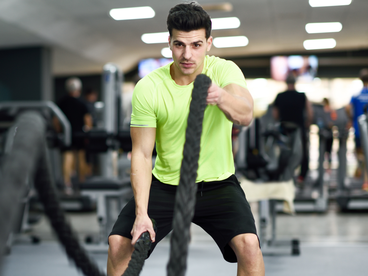 Photo of middle aged male in a bright green shirt participating in a group exercise class using battle ropes
